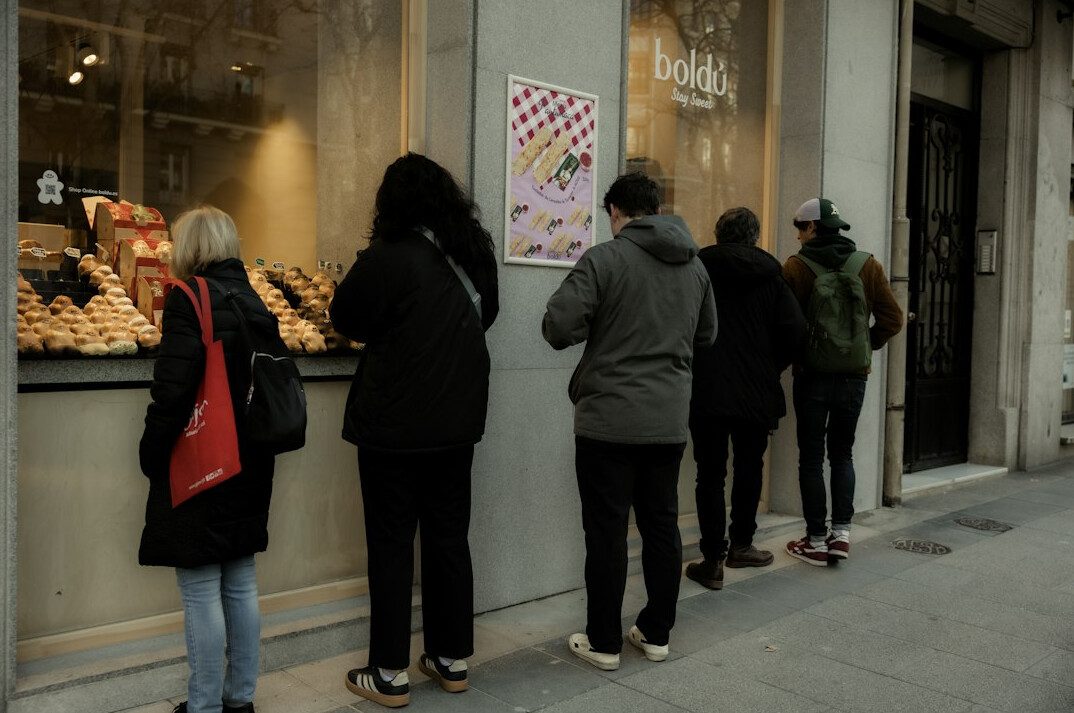 Long queue of people waiting outside a bakery with pastries in the window