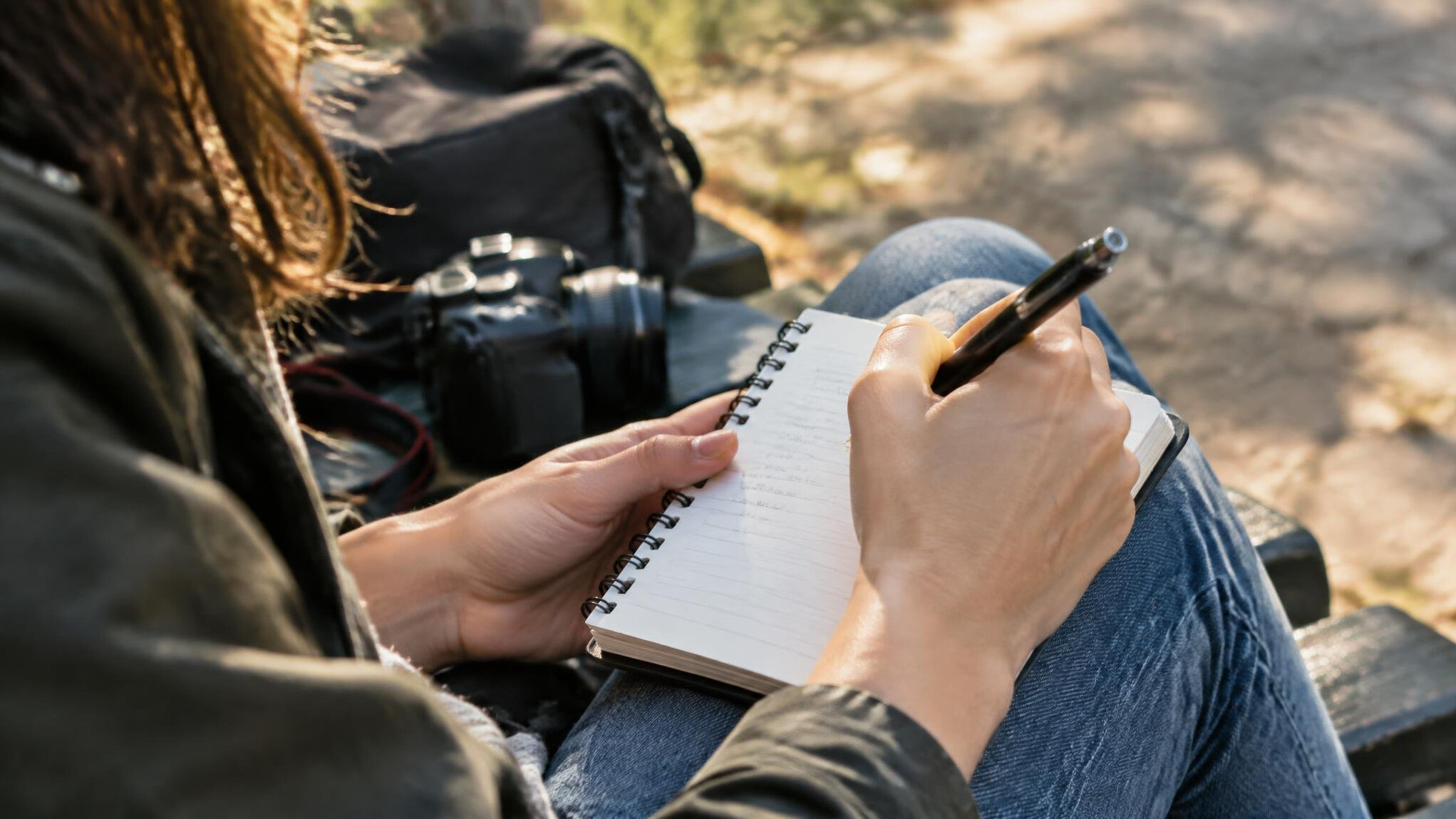 A person writing notes in a notebook while interviewing someone outdoors
